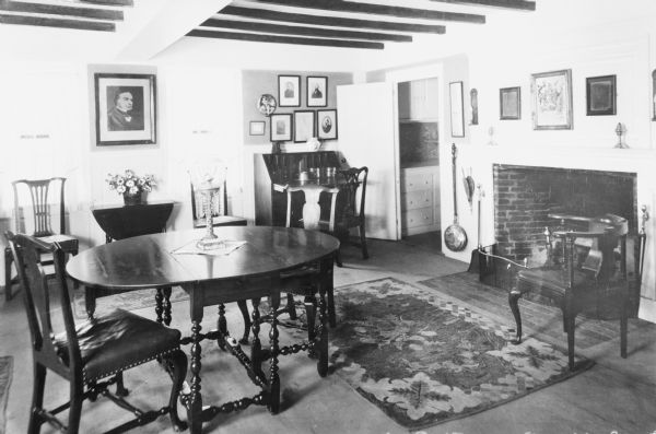 Interior view of Longfellow's Wayside Inn, which opened in 1716. The parlor features a fireplace, beamed ceiling, and paintings.