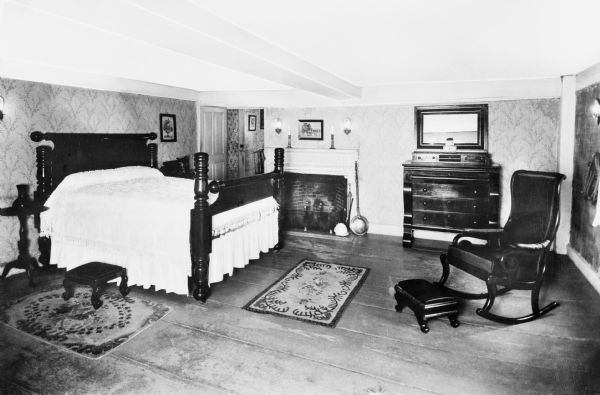 Interior view of Longfellow's Wayside Inn, which opened in 1716. The bedroom features a fireplace, rocking chair, and an elaborately decorated bed.