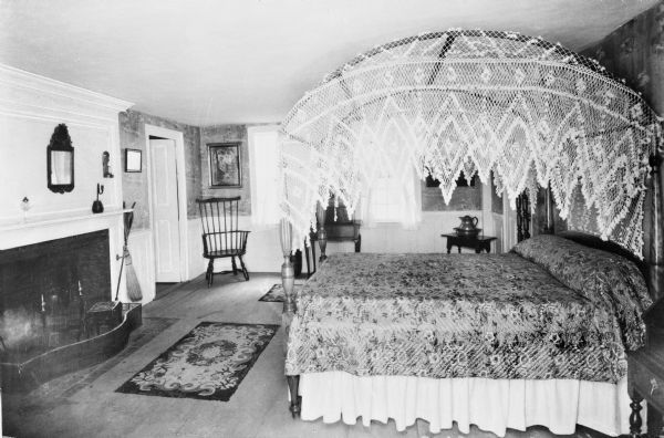 Interior view of Longfellow's Wayside Inn, which opened in 1716. The bedroom features an imposing fireplace and an intricate canopy on the bed.