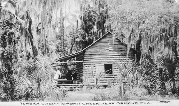 Exterior view of Tomoka Cabin situated on Tomoka Creek. A group of people is sitting at a table on the porch.