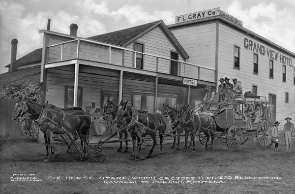 View of a six horse stage which crosses Flathead Reservation Ravalli to Polson, Montana. F.L. Gray Company and Grand-View Hotel can be seen in the background. Published by M.J. Elrod.
