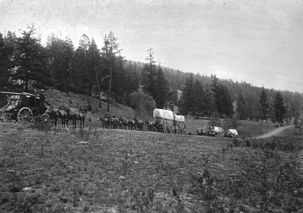 View from field of a stagecoach and a wagon train meeting on a trail in British Columbia, Canada.