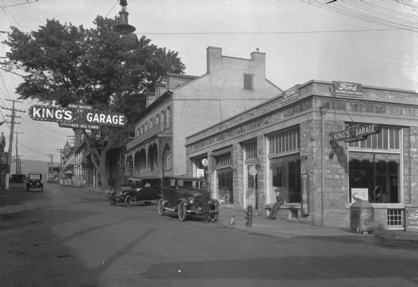 Exterior view of the King Motor Company Garage. Automobiles are parked near the curb, and other cars are being driven down the street.