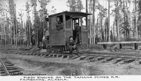 Several men pose on a small locomotive, which was the first engine on the Tanana Miles Railroad. Caption reads: "First Engine On The Tanana Mines R.R. Fairbanks, Alaska."
