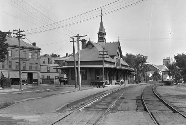 View down railroad tracks of the Leominster Railroad Depot. A boy can be seen riding his bicycle on the platform. Beyond the station stands Columbia Hotel, built around 1892.