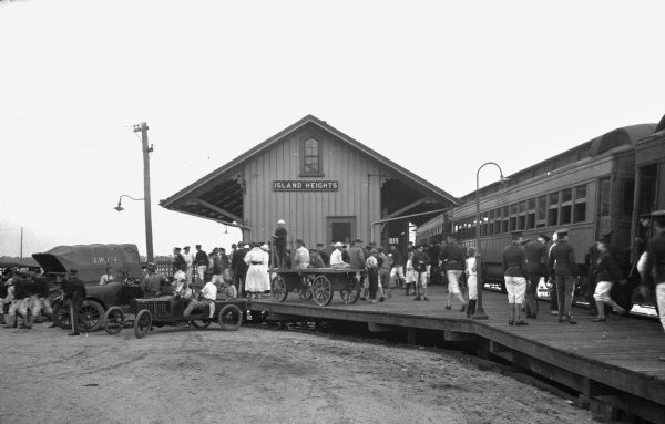 A crowd of children and adults gathers on an elevated boardwalk outside Island Heights Railroad Station, built around 1883.