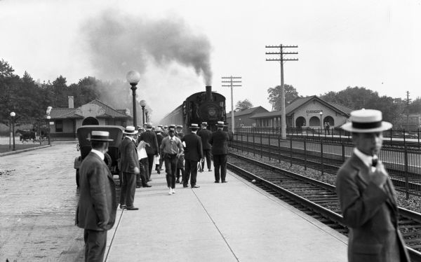 View down railroad platform of crowd of people waiting at the Ridgewood Depot, built in 1916 by architects W.W. Drinker and Frank A. Howard.