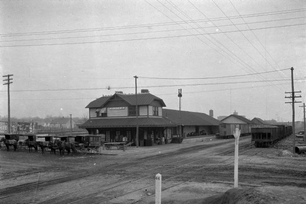 Exterior view of Orangeburg Railroad Station with horse-drawn omnibuses waiting near the tracks.