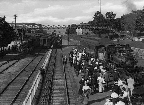 Elevated view of a crowd boarding a passenger car at the railroad depot.