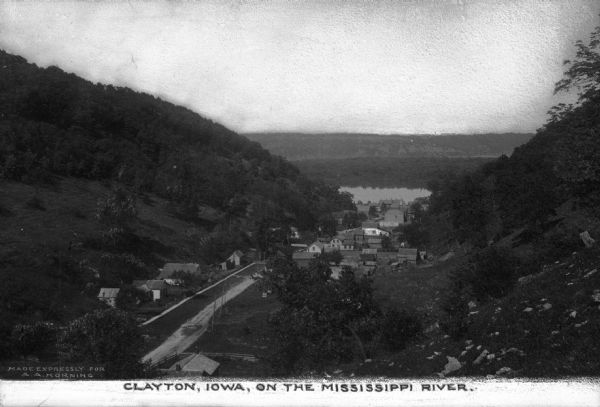 An elevated view of the town of Clayton, Iowa, which is nestled in a valley. The Mississippi River can be seen nearby. Caption reads: "Clayton, Iowa, on the Mississippi RIver."
