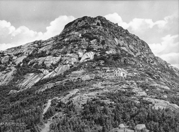 A distant view of a house built on the rocky slope of a mountain.