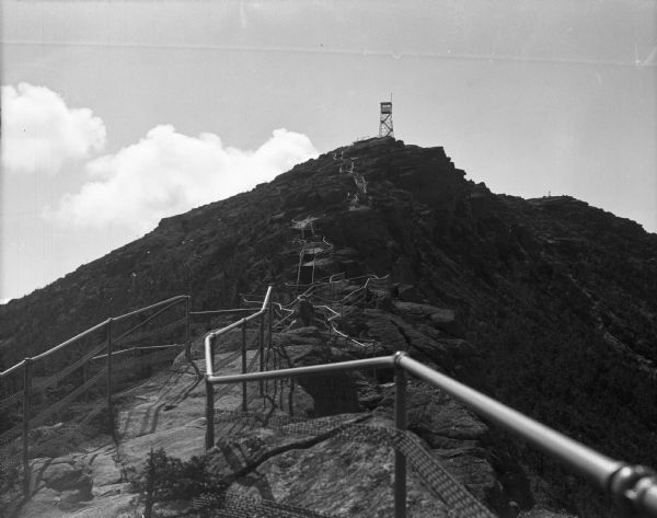 View of a winding path with metal handrails leading up the side of a mountain to a fire lookout tower.