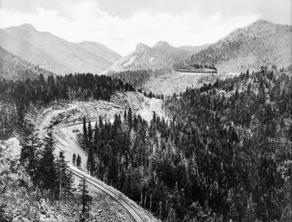 A distant view of the Cripple Creek Short Line Railroad and a train winding through the mountains, circa 1930.