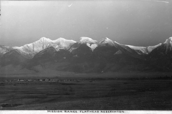 A distant view of the Flathead Reservation and the snow-capped Mission Mountains. Caption reads: "Mission Range Flathead Reservation."