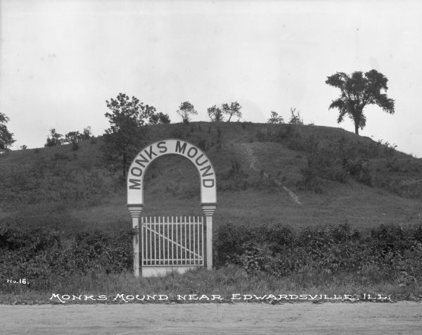View of a gate and sign at Monks Mound, an archaeological site. Caption reads: "Monks Mound near Edwardsville, Ill."