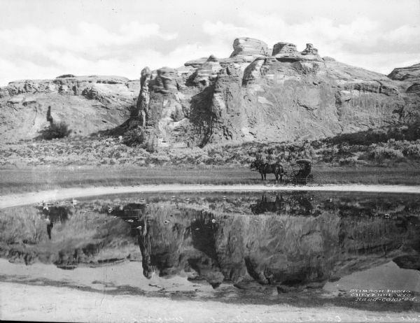 View across salt pool toward a horse-drawn carriage near the far side of the pool, with a rock formation in the distance.