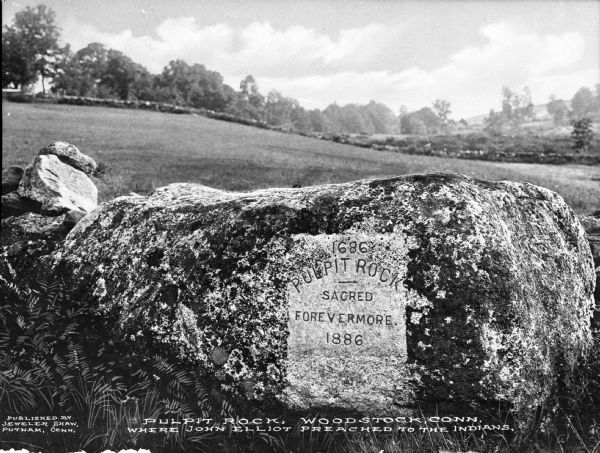 A view of Pulpit Rock, where John Eliot preached to Native Americans. Text etched into the rock reads: "1686 Pulpit Rock -- Sacred Forevermore. 1886." Caption reads: "Pulpit Rock, Woodstock, Conn. Where John Elliot preached to the Indians."