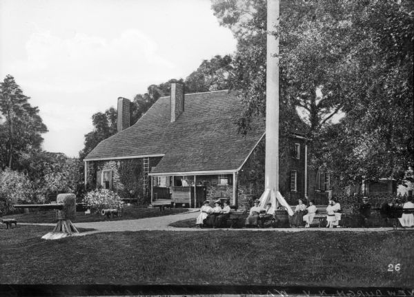 View of a home which was once General George Washington's headquarters, with people sitting on benches outside along a sidewalk. There are cannons on the lawn.