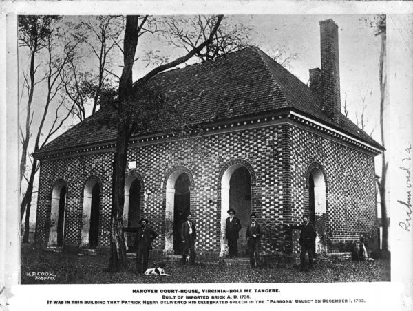 The building in which Patrick Henry delivered his celebrated speech on the "Parson's Cause" on December 1st, 1763. The building itself was made of imported brick A.D. 1735. Five men and one dog are posed in front of the building. Caption reads: "Hanover Court-House, Virginia-Noli Me Tangers. Built of imported brick A.D. 1735. It was in this building that Patrick Henry delivered his celebrated speech in the 'Parsons Cause' on December 1, 1763."