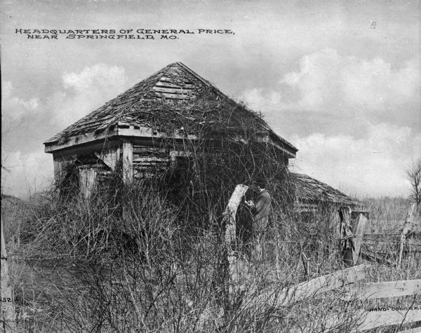 A view of a man standing in front of the ruins of General Sterling Price's former headquarters. Price served as a United States Army brigadier general during the Mexican-American War, and a Confederate Army major general in the American Civil War. Caption reads: "Headquarters of General Price, near Springfield, MO."