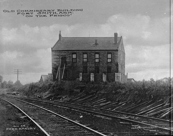An old commissary building situated behind railroad tracks. Caption reads: "Old Commissary Building Fort Smith, Ark., 'On the Frisco'."
