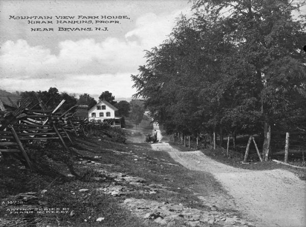 View along country road toward a farm house. There is a man driving a horse-drawn wagon on the road. A fence lines the road on the left. Caption reads: "Mountain view Farmhouse, Hiram Hankins Propr., near Bevans N.J."