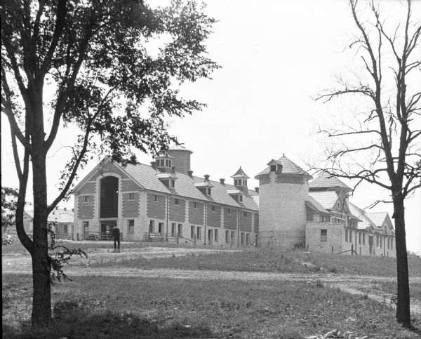 View across grounds toward a man standing in front of an enormous commercial barn on Mr. Barber's farm.