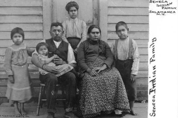 A group portrait of a Seneca Native American family, with a man, woman, four children, and a kitten. Caption reads: "Seneca Indian Family, Salamanca, N.Y."