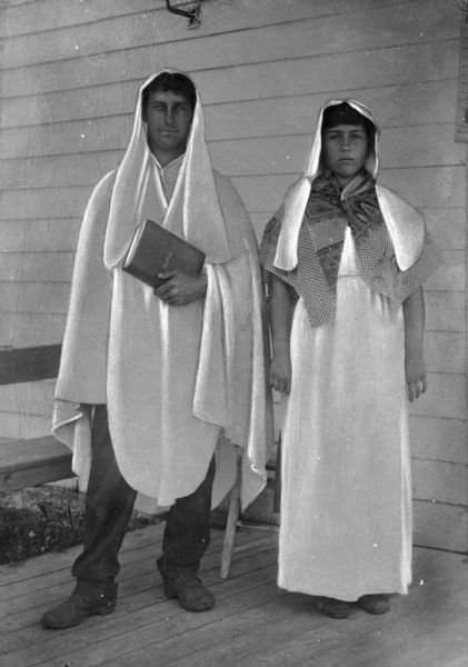 A view of a boy and a girl clad in "costumes worn by brothers and sisters". The boy on the left is holding a Bible in his left hand.