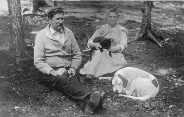 A man and woman relaxing in the Adirondack Mountains in New York State. The woman is holding a cat, and a dog is curled up near her feet.