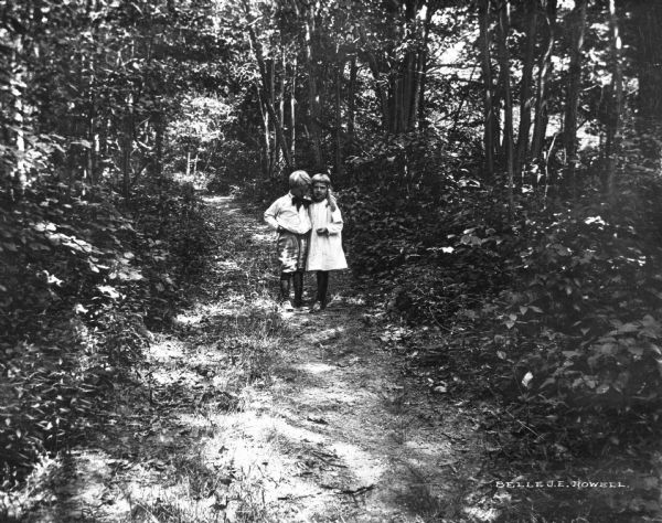 A view of a little girl and boy embracing on a densely wooded path.
