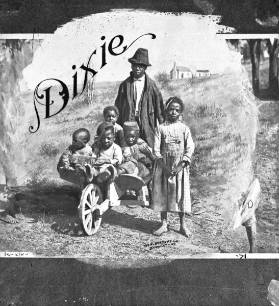 A view of six African American children, with four children sitting in a wheelbarrow and two children standing next to them. A house is in the far background. Caption reads: "Dixie."