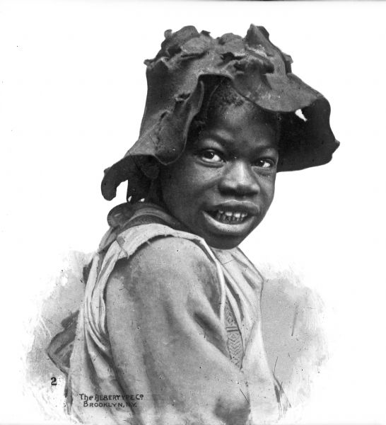 A portrait of an African American child wearing a tattered hat against a white background.