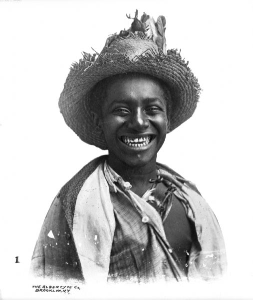 A portrait of an African American boy wearing a straw hat against a white background.