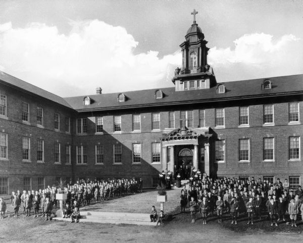 A view of the exterior of St. Michael's Industrial School, with teachers and students gathered in front of the building.