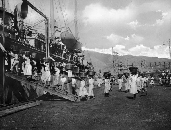 Women loading cargo onto a U.S. ship at St. Thomas in the Virgin Islands by way of baskets balanced on the tops of their heads.