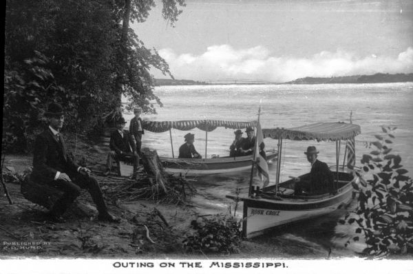 View from shoreline toward two small excursion boats with six men and one boy stopped for a rest along the shore of the Mississippi River. Caption reads: "Outing on the Mississippi."