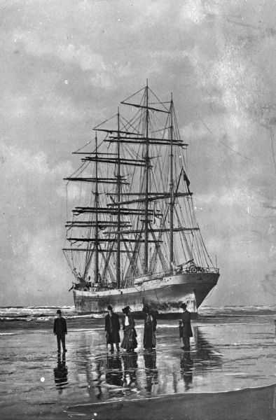 A bark, the "Galena," stranded on Clatsop Beach, with three men and two women on the beach in the foreground.