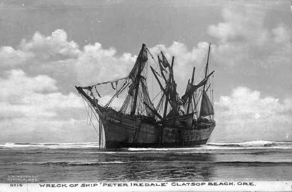 A view of the wrecked ship beached in shallow water. The ship ran ashore in 1906. Caption reads: "Wreck of Ship 'Peter Iredale' Clatsop Beach, Ore."