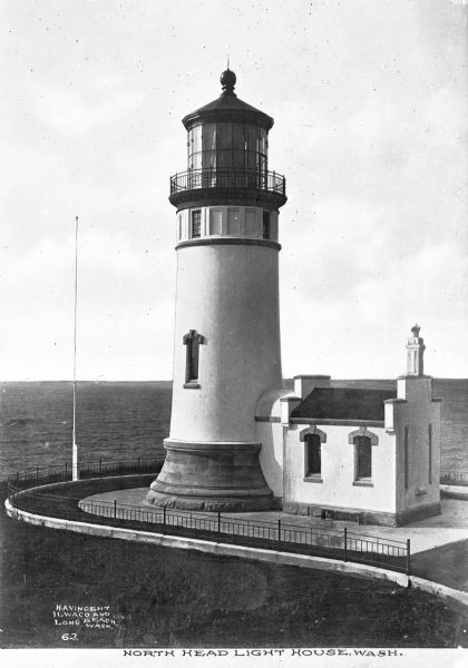 Elevated view of the century-old North Head Lighthouse, completed in 1898, built in response to a marked increase in the number of shipwrecks along the Peninsula as mariners coming from the north could not see the Cape Disappointment light. The 65-foot North Head Lighthouse was designed by German-born engineer C.W. Leick and sits on solid basalt more than 190 feet above sea level. It first used the hand-me-down first order Fresnel lens from Cape D, switching to search light and finally beacon light at the same time changes were made to her sister lighthouse in 1939. Caption reads: "North Head Light House, Wash."