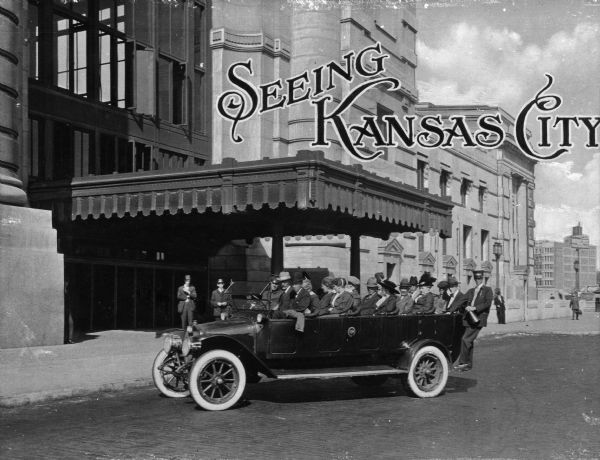 View from street looking toward a touring car filled with tourists outside of a building lobby with a roof over the sidewalk. Caption reads: "Seeing Kansas City."