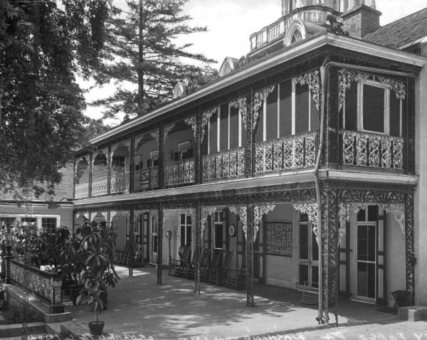 View of the exterior of the Washington Inn, including screened-in second-floor porches and wrought-iron flourishes. A row of chairs is near the ground floor entrance.
