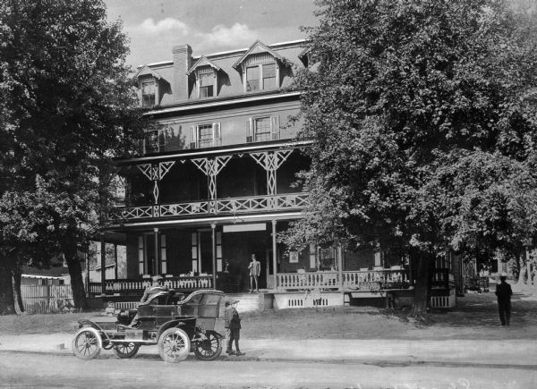 View across road toward the Charter House Hotel. A driver is sitting in an early touring automobile in front, and other people are standing nearby.