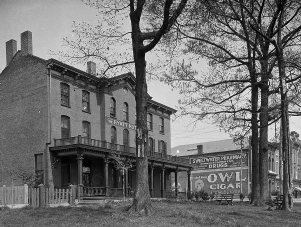 View across yard toward the Hyatt Hotel. There is a sign on a building in the background for the Sweetwater Pharmacy and Owl cigars.
