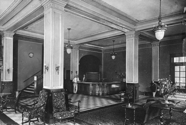 The lobby of the Hotel Emmerson. In the back of the room are two men standing at the front desk. Opened in 1926 as the New Mt. Vernon Hotel, the building quickly became a Mt. Vernon Landmark. The hotel was five stories high, had 150 rooms and rates started at $1.75. Many Mt. Vernon residents remember the "human fly" who climbed the northwest corner of the hotel soon after its opening. The hotel was considered fire-proof because there were no wooden floors or walls in its construction. Between 1929 and 1933 the hotel changed its name to Emmerson in honor of the Illinois governor of that time, Louis Emmerson. In 1983 the hotel was demolished after remaining vacant for a short time and was replaced by a parking lot.