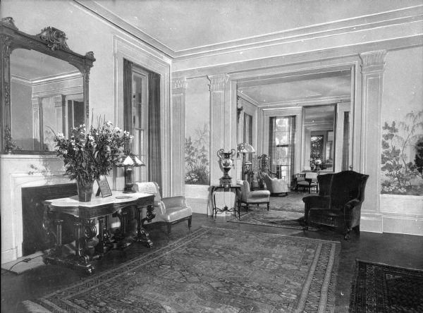 A view of the main rooms of the Boxwood Manor. On the left is a flower arrangement on a table in front a large mirror.