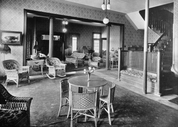 A view of the lounge at the Hotel Mahohae, arranged with tables and wicker chairs. There is a staircase on the right behind a built-in bench.