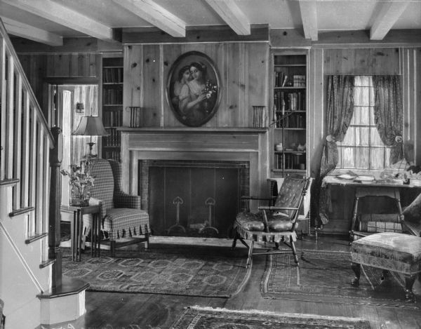 A view of the Militon Court Inn's lounge with a staircase in the left foreground, and a fireplace, chairs, a painting, and books on shelves.