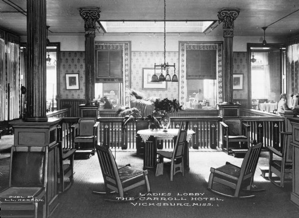 The ladies lobby at the Carroll Hotel, named for Capt. E.C. Carroll, filled with tables, chairs, and plants. The Carroll Hotel was razed in the 1960s to make space for a parking garage. Caption reads: "Ladies Lobby, The Carroll Hotel, Vicksburg, Miss."