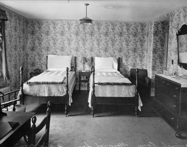 A bedroom at the Norwich Inn, featuring two beds, a dresser, mirror, desk, chairs, and a nightstand. Built in 1929, the original Norwich Inn was a haven for the rich and famous of the day, drawing such luminaries as George Bernard Shaw, Charles Laughton, Frank Sinatra, and the Prince of Wales. The classic Georgian Colonial revival structure, with its handsome front portico, door, and fanlight, included 75 guestrooms and boasted an expansive, rolling golf course.